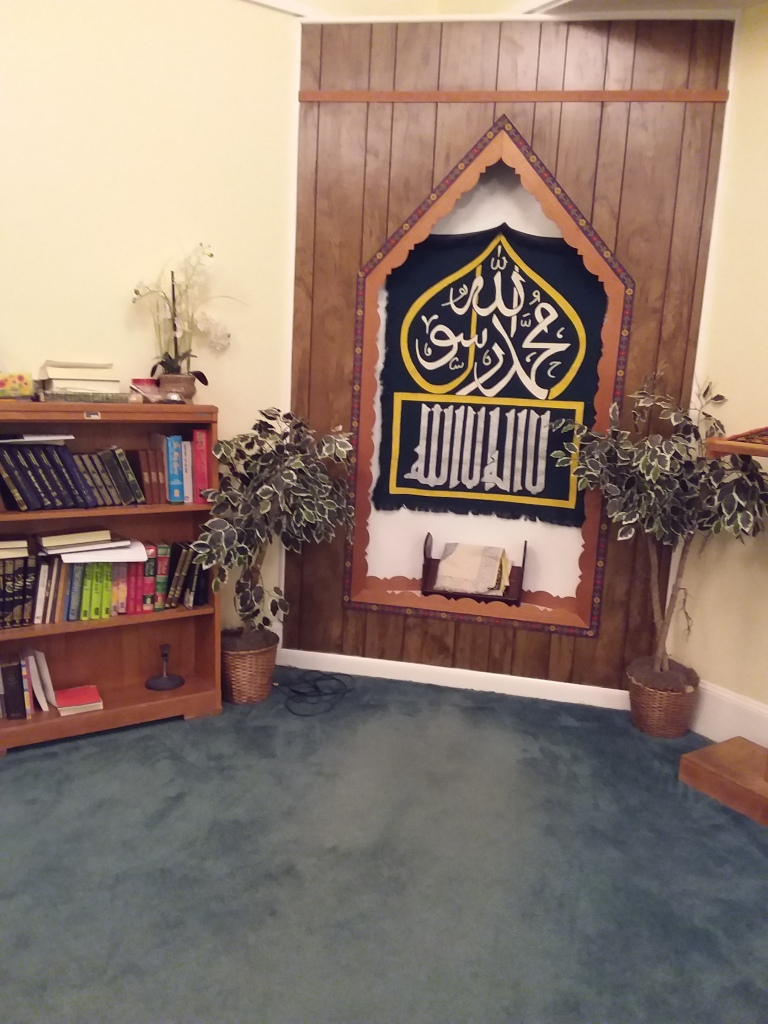 This image shows the inside of the Ar-Razzaq Islamic Center including a book case, plants, and...